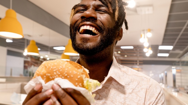 young man laughs while holding a burger