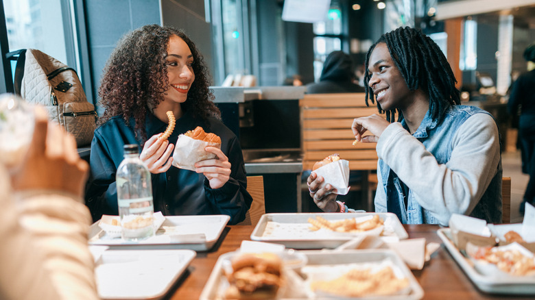 Two friends smiling as they eat fast food at restaurant table.