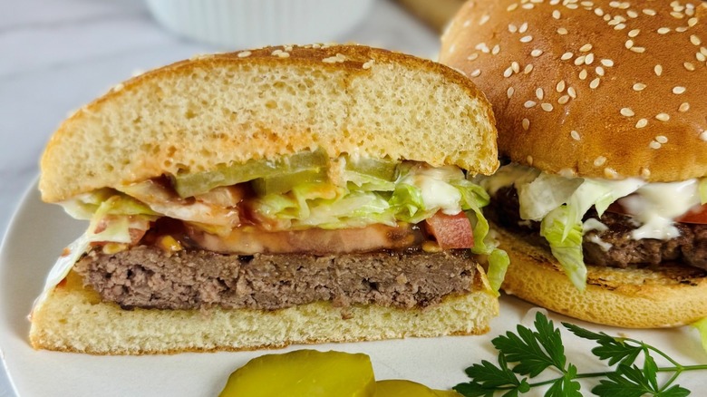 whole burger next to half a hamburger with pickles and parsley on a plate