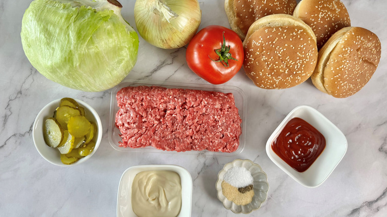 ground meat, produce, cheese, and buns laid out on a marble surface
