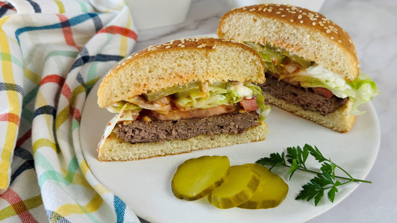 two halves of a hamburger on a white plate with three dill pickle slices