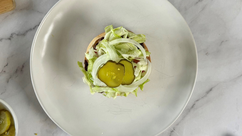 burger patty and vegetables on a bun on a white plate