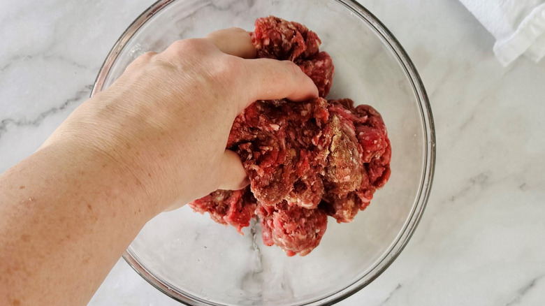 hand squishing ground meat in a clear bowl