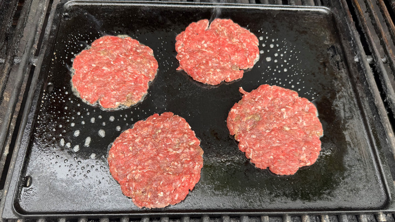 four raw burger patties on a propane grill sizzling