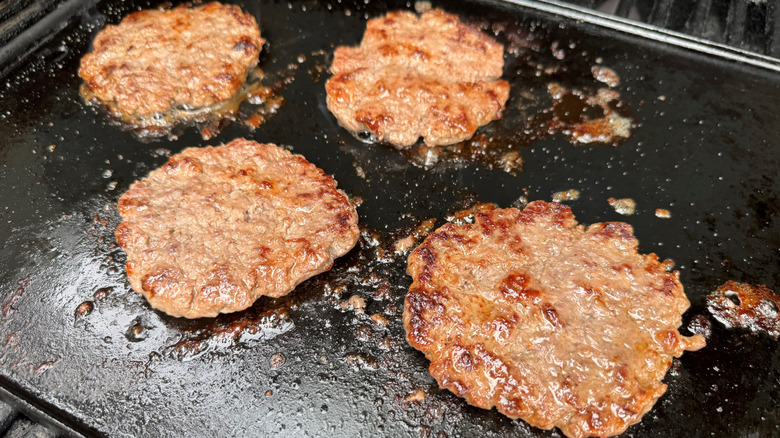 four cooked burger patties on a propane grill