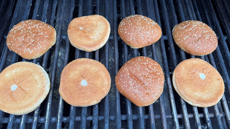 two rows of hamburger buns face down on a propane grill