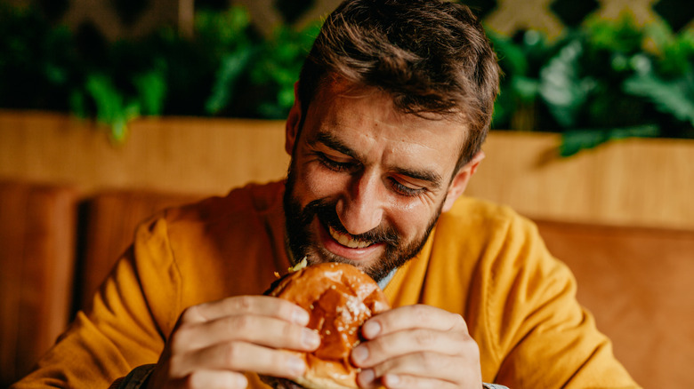 Smiling man eating burger while sitting