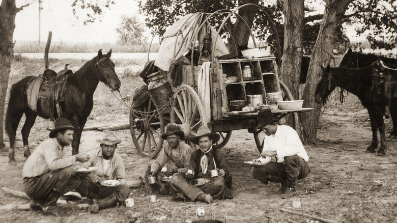 19th century cowboys eating next to a chuck wagon