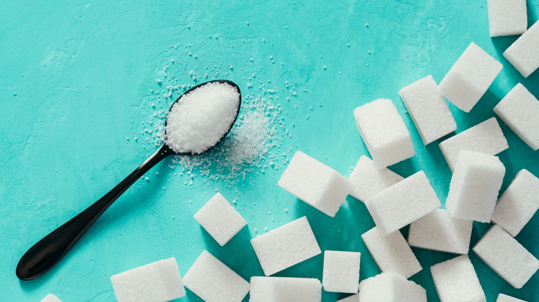 Sugar in spoon and sugar cubes on blue background
