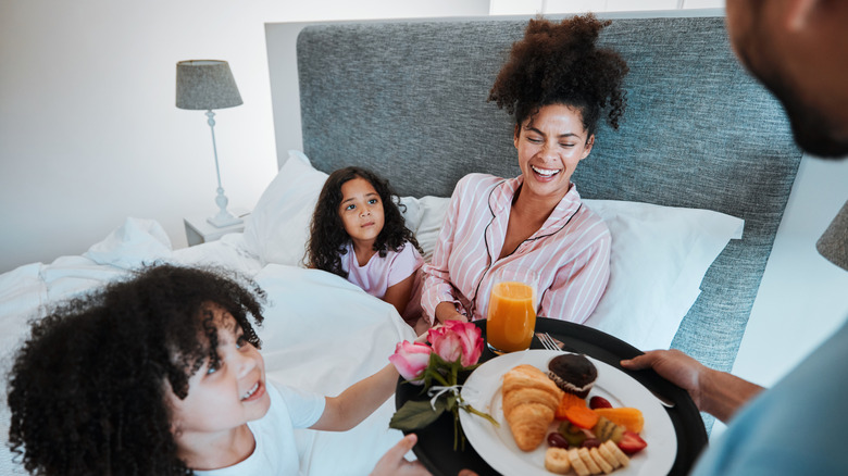 Mother being served breakfast in bed with children sitting next to her.