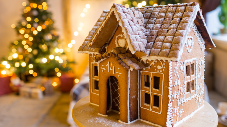 Decorated gingerbread house with blurred Christmas tree in background.