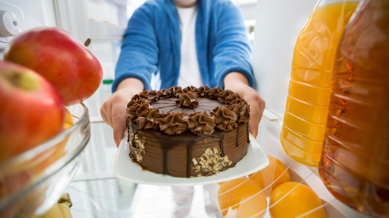 Man placing chocolate cake inside fridge