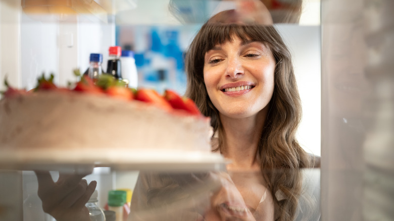 Woman putting cake in open fridge