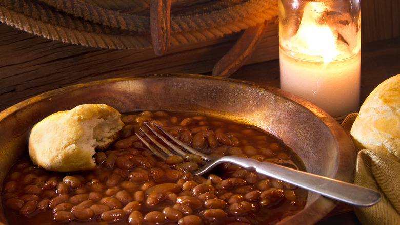 Closeup of baked beans and biscuits with rope, horseshoe, and candle in background