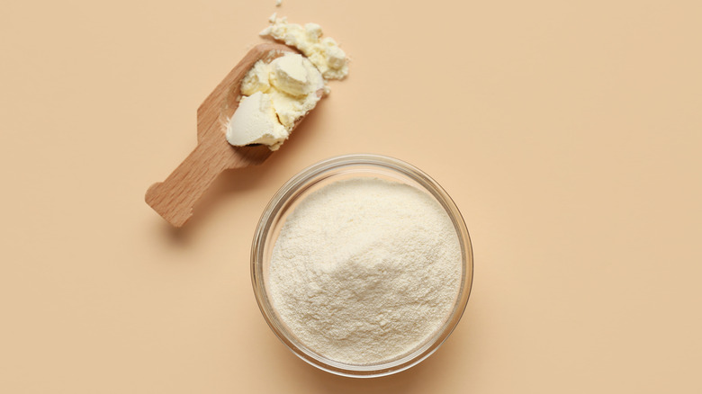 A bowl of milk powder and a wooden scoop on a beige background