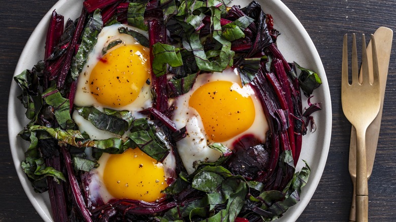 Beet greens in a bowl with three fried eggs.