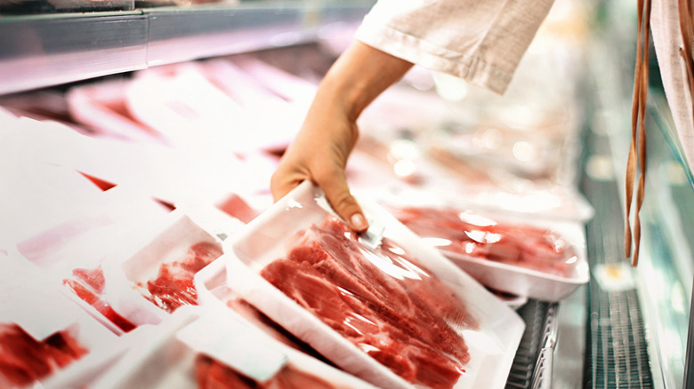 Someone picking up a tray of meat in a supermarket