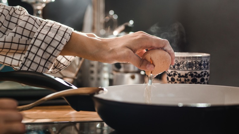 hand cracks an egg into a skillet
