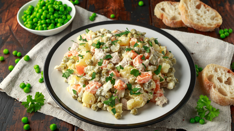 plate of spanish ensaladilla rusa beside a bowl of peas, sliced baguette