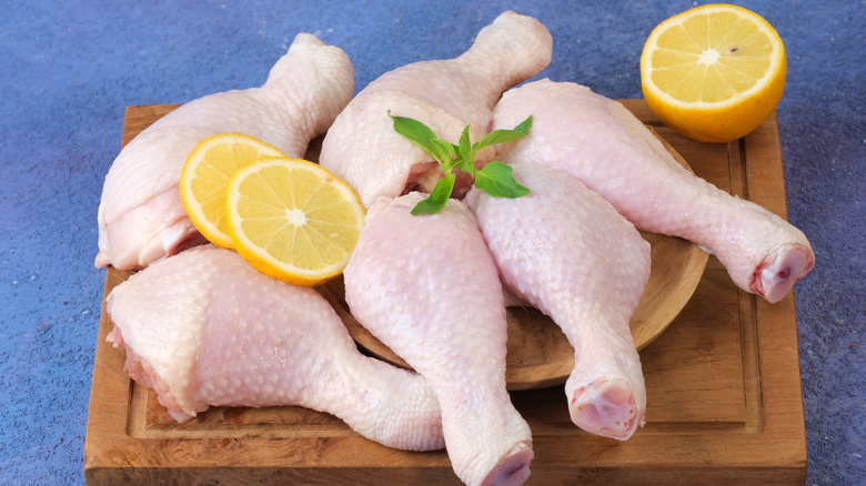 Raw chicken drumsticks with lemon on a wooden chopping board