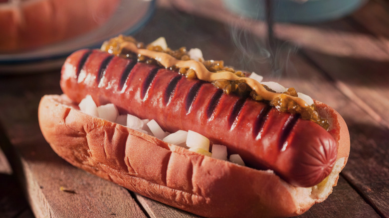 Steaming hot grilled hot dog on a bun with mustard, relish and onions.