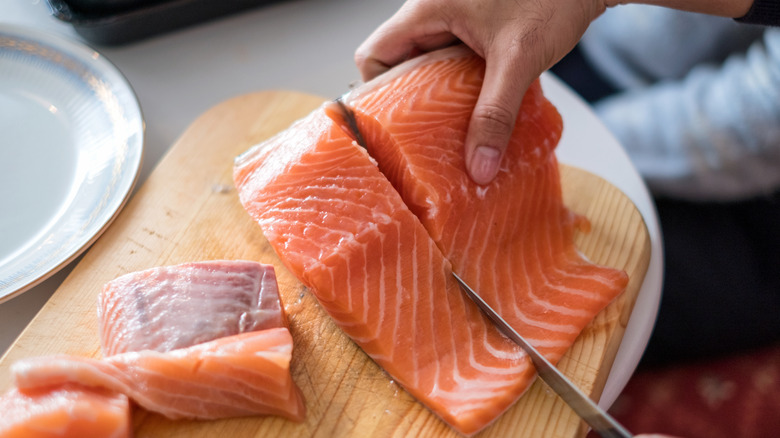 Person cutting raw salmon on board.