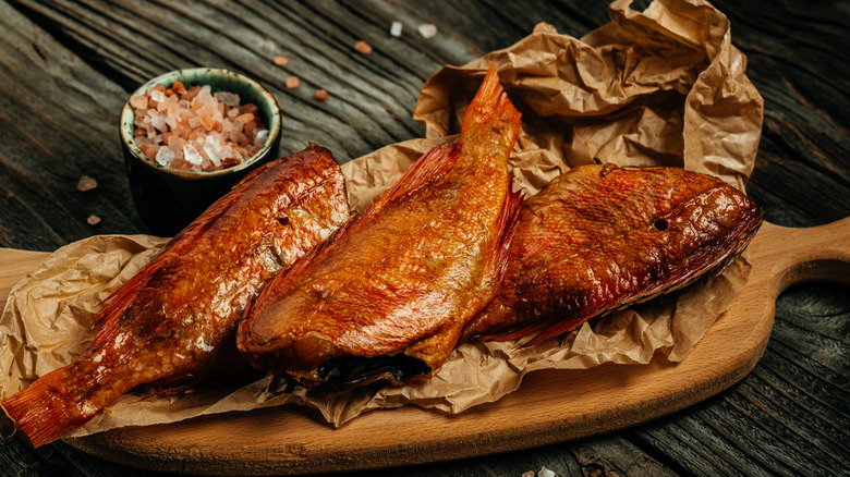 Three smoked fish on a wooden board.