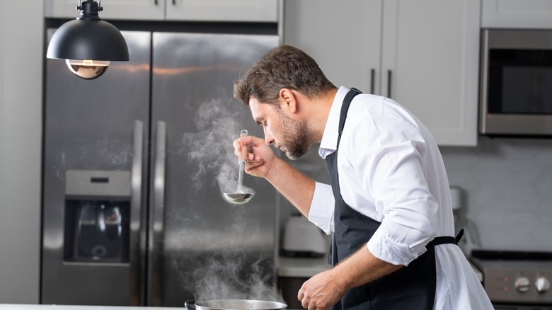 a man in an apron tastes soup on the stove