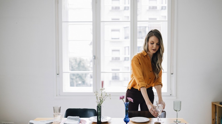 woman sets a table in a white dining room
