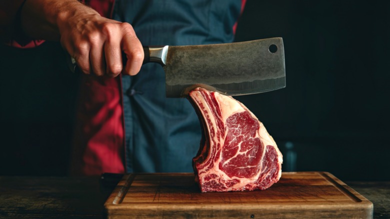 person in apron with cleaver and raw prime rib roast