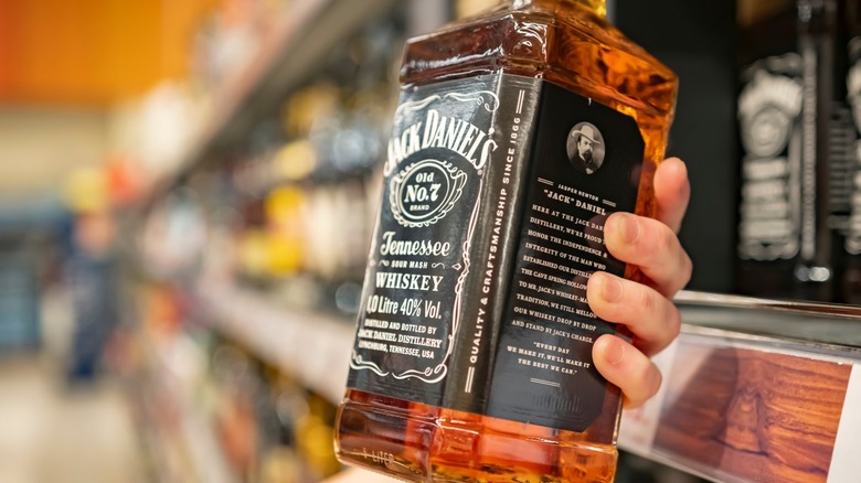 a hand holds a bottle of jack daniel's in a store