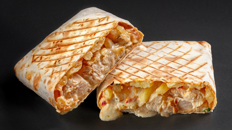 A French tacos cut in half, filled with meat, cheese sauce, and french fries.