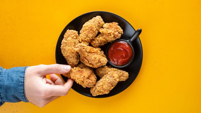 hand reaches for fried chicken on black plate