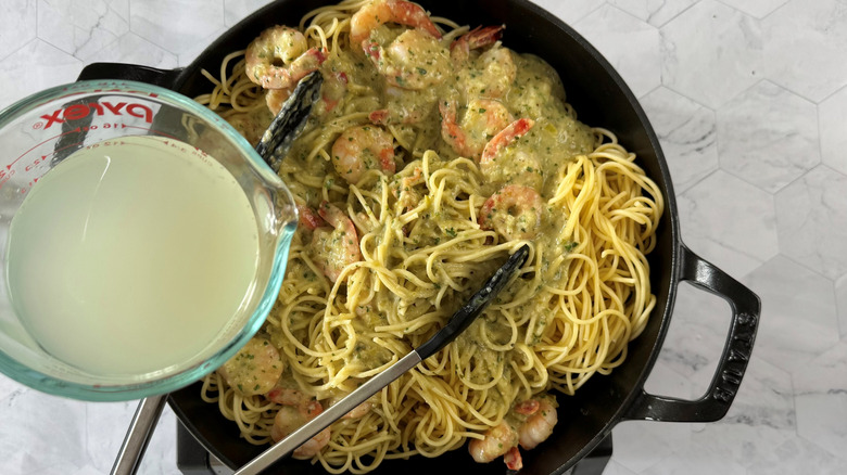 pouring pasta water into pan with spaghetti, prawns, and sauce