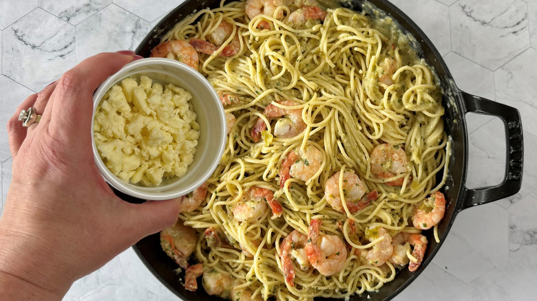 garnishing garlic prawn and tomatillo pasta with cotija cheese