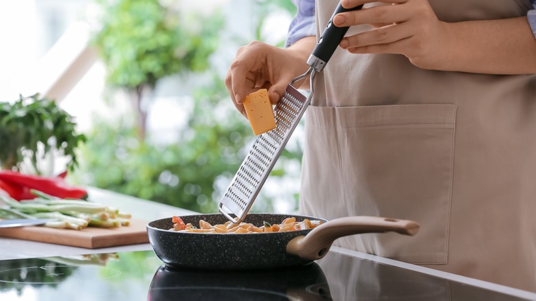 grating cheese over pasta in pan