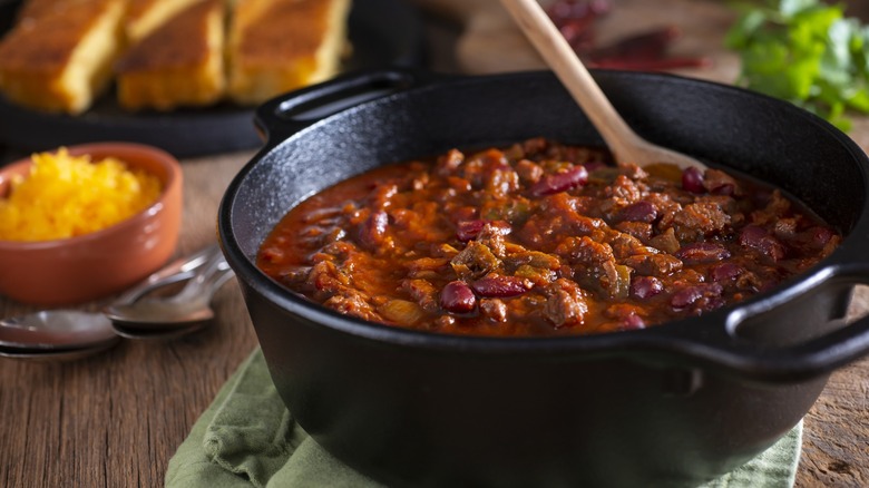 cast iron pot of chili with cornbread and utensils