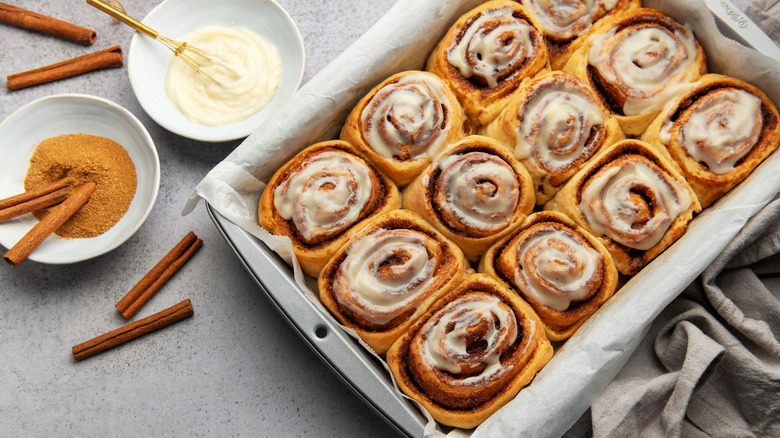 A tray of fresh cinnamon rolls next to two small bowls filled with cinnamon powder and icing