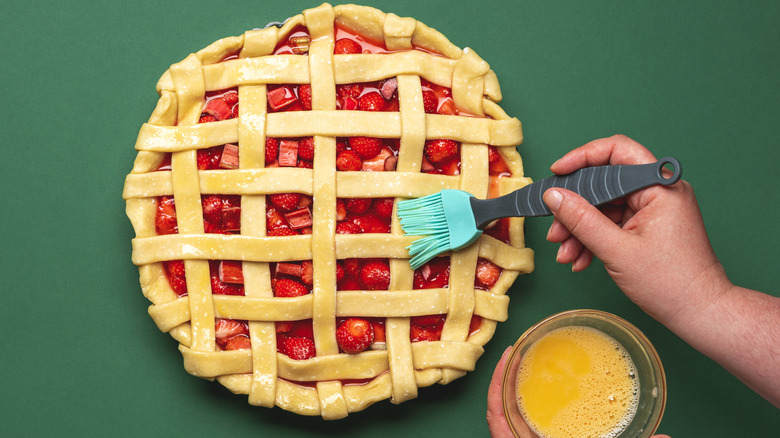 Top-down view of adding egg wash to a cherry lattice pie