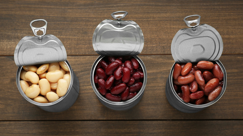 Three open cans of beans on a wooden table