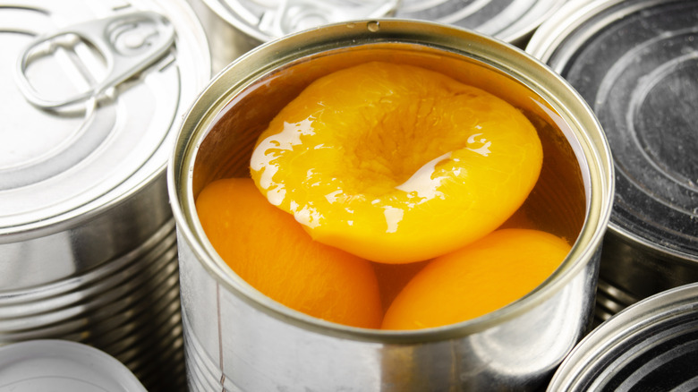 An open can of peaches surrounded by closed tin cans