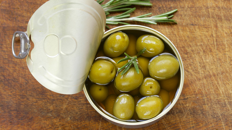 An open can of green olives garnished with rosemary
