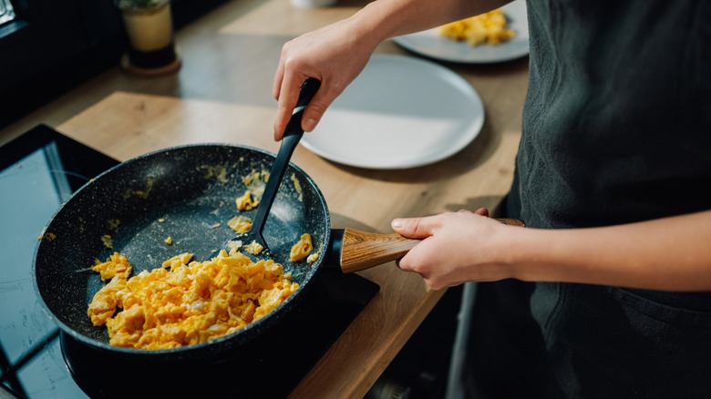 hands scramble eggs in a skillet