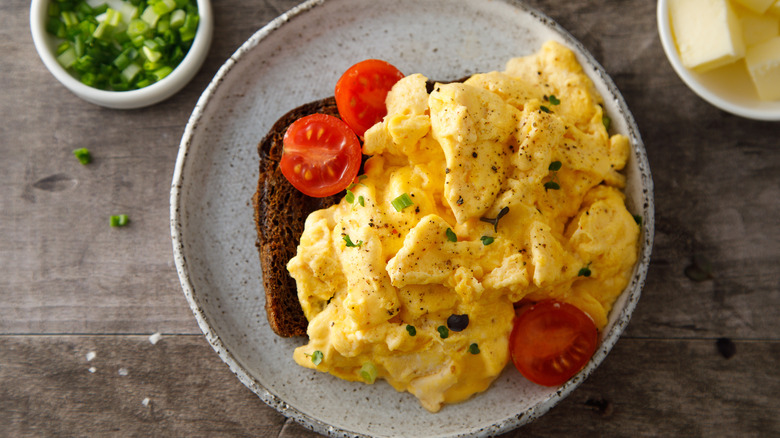 Top-down view of a plate of scrambled eggs with fresh tomatoes