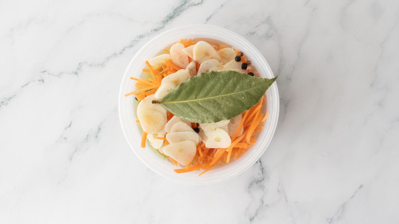 Various sliced veggies and bay leaf in container