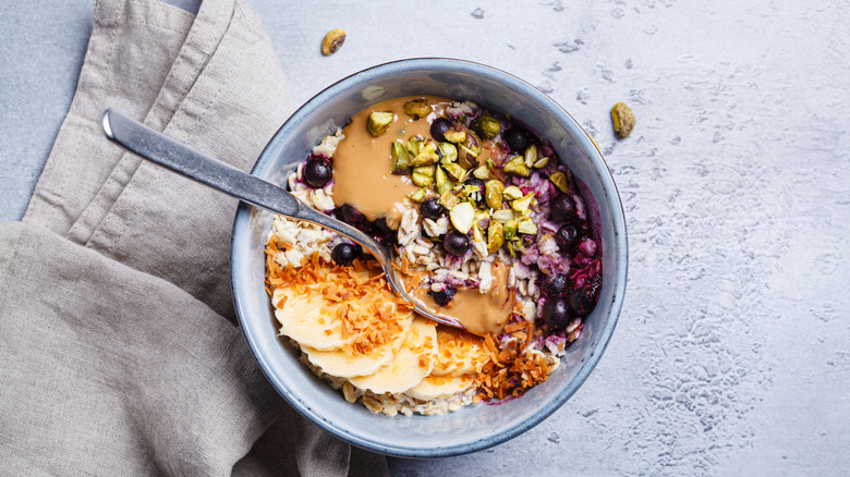 A protein-filled bowl of oatmeal with berries, bananas, peanut butter, and nuts on a gray background