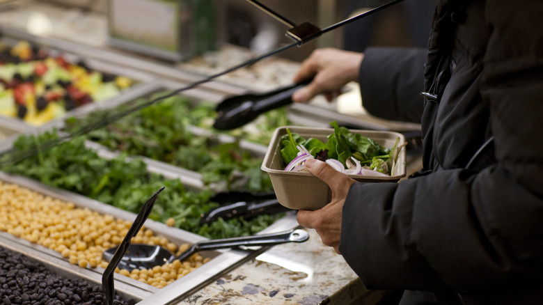 Person filling container with items from salad bar