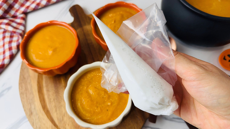 Hand holding piping bag full of milk over bowls of soup