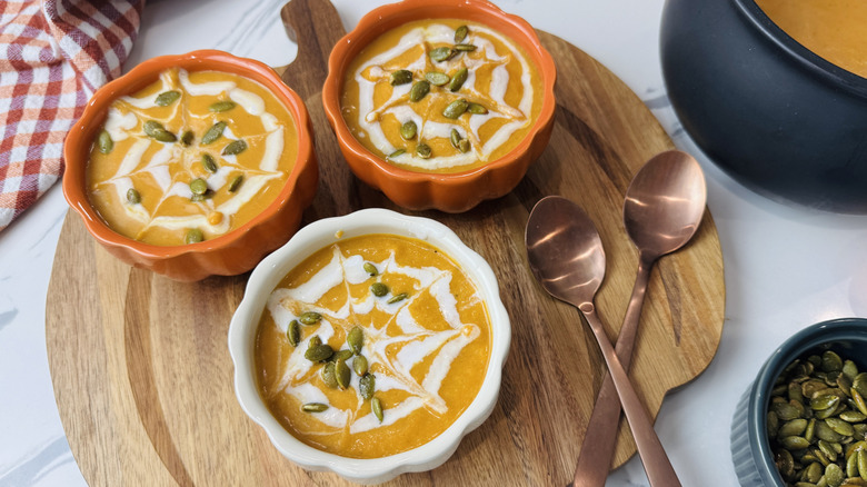 Bowls of pumpkin soup with coconut milk spiderweb designs and pepitas