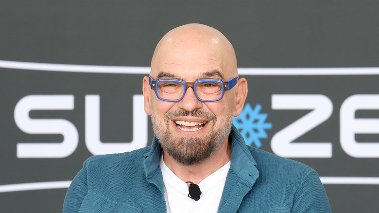 Michael Symon smiling wearing blue glasses.